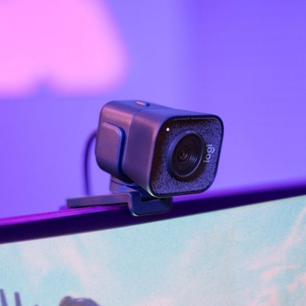 Vue de trois quarts webcam streaming Logitech StreamCam grise installée sur le haut d'un écran PC avec éclairage violet FlowUP