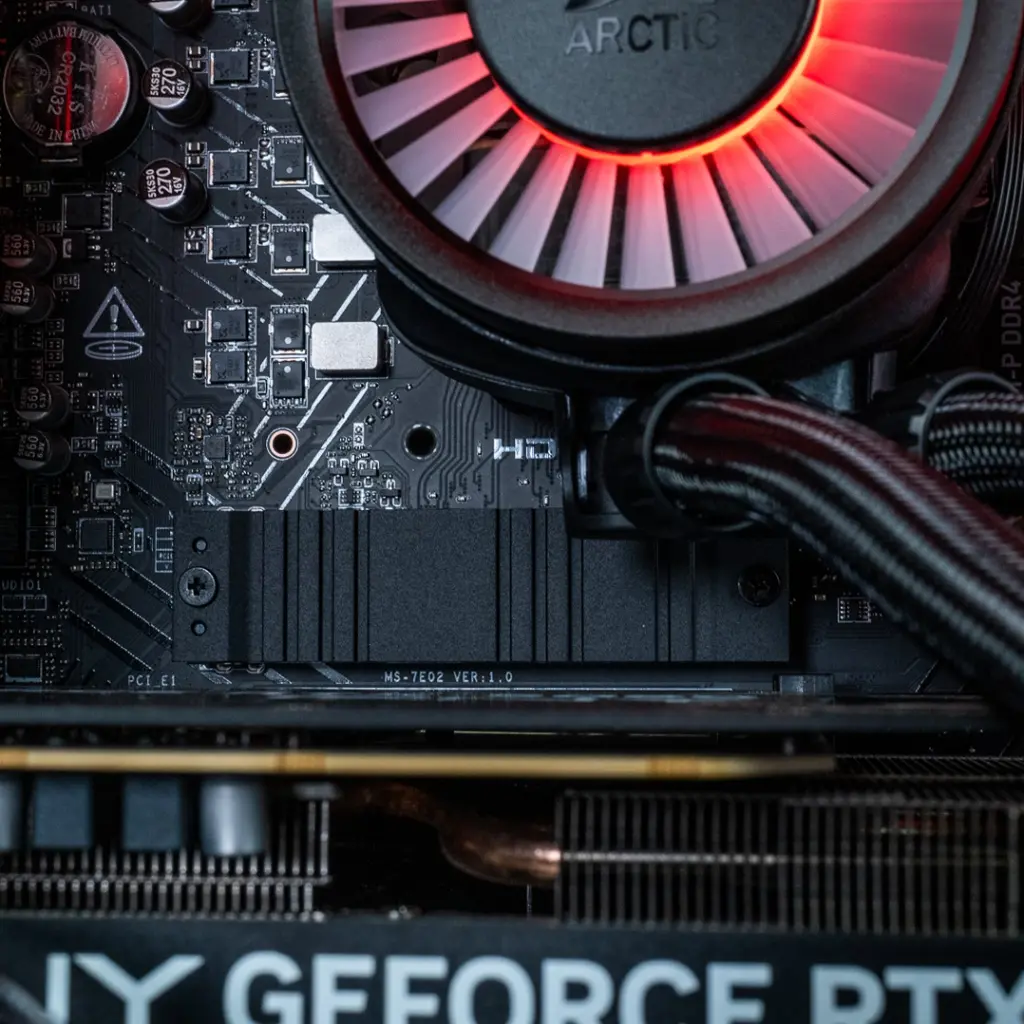 Gros plan sur le dissipateur thermique noir du SSD NVMe et le ventilateur du waterblock Arctic avec éclairage ARGB rouge à l'intérieur du PC Gamer Banger