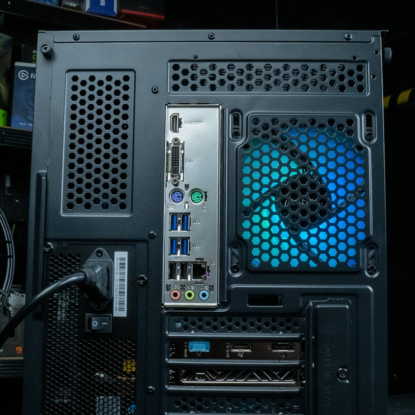 Vue arrière du PC gamer Nightwing mettant en évidence le panneau de connectique complet, l'alimentation avec interrupteur et le ventilateur MSI ARGB bleu à travers la grille en nid d'abeille