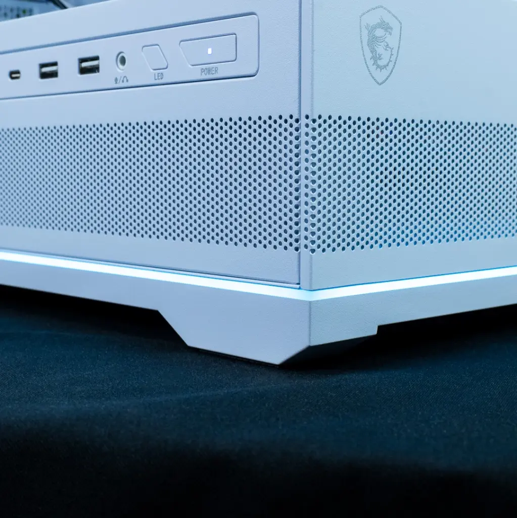 Gros plan sur le coin inférieur du boîtier blanc du PC gamer Rubis, montrant le panneau avant avec les boutons POWER et LED, les ports USB et une prise jack